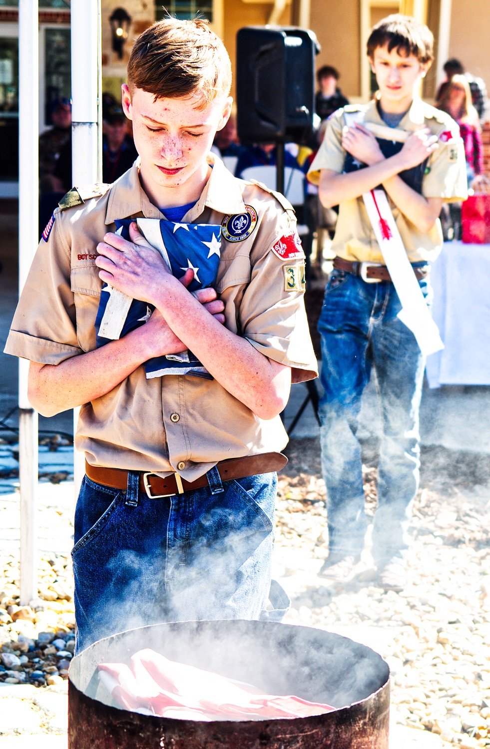 Scouts place American flags onto the pile for retirment as the smoky cylinder of symbols begins to burn.